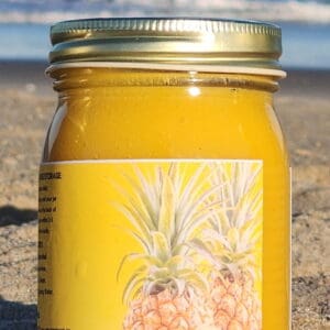 Jar of pineapple juice on sandy beach.